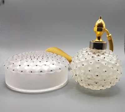 a glass perfume bottle with a gold handle and a glass jar with a lid