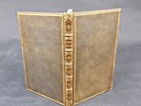 an old book with a gold cover and gold trim on a gray background