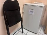 une chaise noire et un réfrigérateur blanc dans une petite pièce