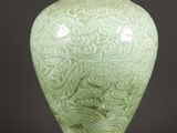un vase vert posé sur une table, devant un fond noir