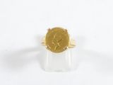 bague en or jaune surmontée d'une pièce, posée sur un fond blanc