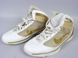 une paire de baskets de basket-ball Nike blanches et dorées posées sur une surface blanche