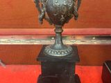 un vase en bronze sur un piédestal sur une surface rouge