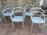 four white chairs sitting next to each other on a brick floor