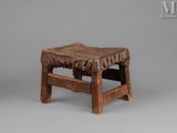 an old wooden stool with a leather seat on a gray surface