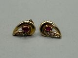 une paire de boucles d'oreilles en or et rubis posées sur un fond blanc