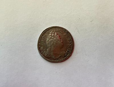 une pièce d'argent sur laquelle est représentée une couronne, posée sur une surface blanche