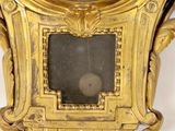 a gold clock with a black face on a white wall