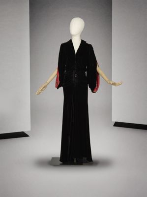 une photo d'un mannequin vêtu d'une robe noire et d'une cape rouge