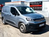 La camionnette argentée est garée devant un immeuble sur le côté duquel est accrochée une pancarte.