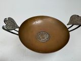a metal bowl with two birds on it on a table