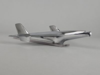 maquette d'avion en métal argenté posée sur une surface blanche, avec un fond gris