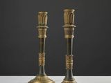 une paire de bougeoirs anciens en laiton posés sur une table blanche