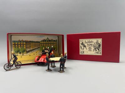 deux figurines représentant des personnages, dans une boîte rouge ornée d'une illustration représentant une calèche