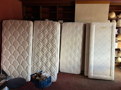 Plusieurs matelas sont alignés dans une pièce où se trouve une étagère sur laquelle sont posés d'autres matelas