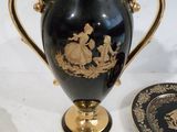 un vase noir muni d'une anse dorée et une assiette décorée d'un motif