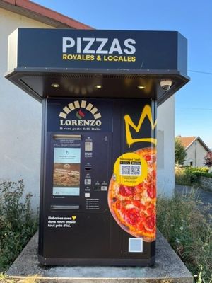 un distributeur automatique sur lequel est posée une pizza, devant un immeuble