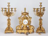 three gold colored candlesticks and a clock on a table