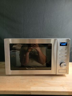 une personne en train de se prendre en photo dans un micro-ondes posé sur une table en bois