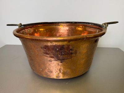 an old copper pot with a handle sitting on a table