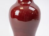 un vase rouge posé sur une surface blanche