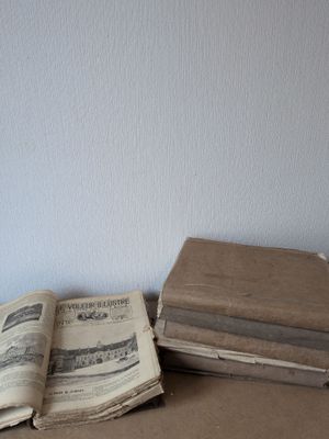 Plusieurs vieux livres sont empilés sur une table, avec un mur blanc en arrière-plan.