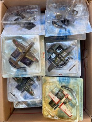 Six petits avions miniatures se trouvent dans une boîte en carton posée sur une table.