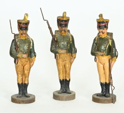 three figurines of soldiers in green and yellow uniforms on wooden bases