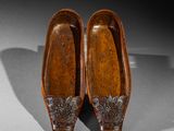 pair of wooden shoes with metal decorations on them on a gray surface
