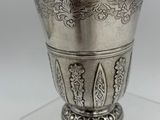 an antique silver cup on a clear stand on a white surface