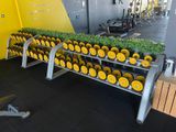 a rack of dumb dumbs in a gym with yellow wheels
