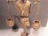 a bronze statue of a man holding a scale and a bucket