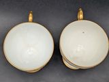 two white cups with gold rims on a black surface