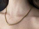 La femme porte un haut noir et un collier à chaîne dorée.