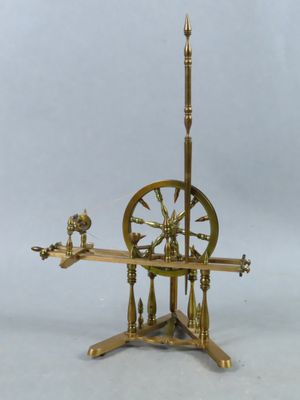 une machine à filer ancienne en laiton, posée sur un socle surmonté d'une horloge