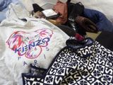 a white t - shirt with a horse on it sitting on a bed next to a pair of shoes and a purse