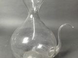 a clear glass vase with a curved handle on a table