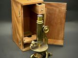 un vieux microscope en laiton avec un coffret en bois sur fond gris