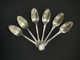 six cuillères en argent sont disposées en rangée sur une surface noire
