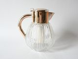 a glass pitcher with a metal handle on a white surface