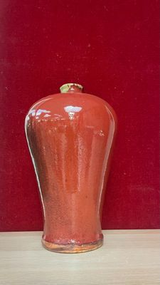a red vase sitting on a table in front of a red wall