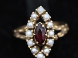 a close up of a gold ring with a red stone surrounded by pearls