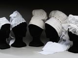 trois têtes de mannequins coiffées de chapeaux et drapées de tissus blancs