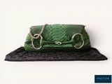 green snake skin purse with gold hardware and chain on a black surface