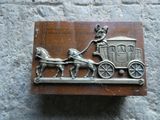 une plaque métallique représentant une calèche tirée par des chevaux, avec un homme à bord
