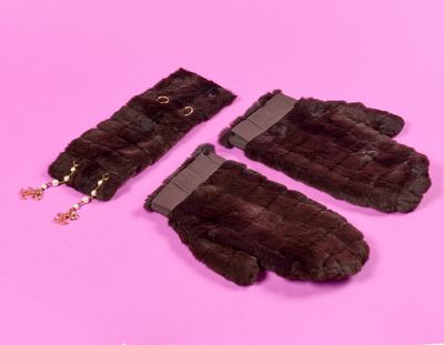 paire de mitaines en fourrure marron sur fond rose, ornées d'une chaîne dorée