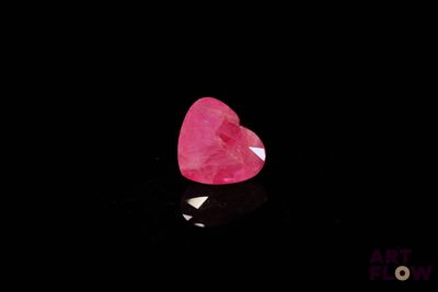 un gros plan d'un diamant rose en forme de cœur sur une surface noire