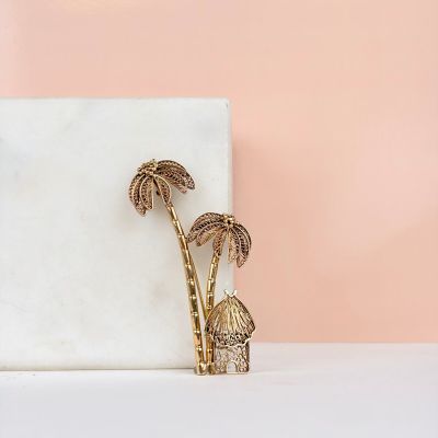 deux broches en forme de palmiers dorés posées sur une surface en marbre blanc