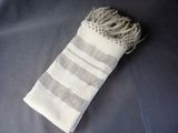 grey and white striped towel with fringes laying on a bed