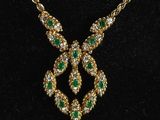 a gold necklace with green and white stones on a black velvet surface